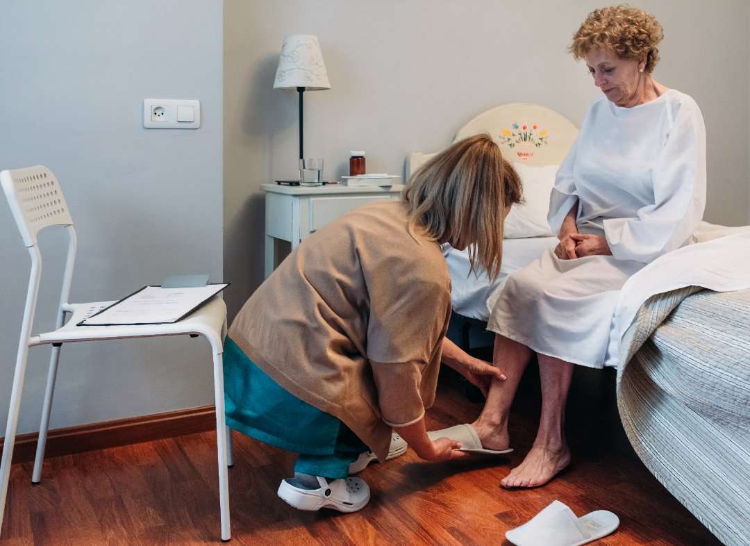 Female carer wearing slippers to elderly female patient